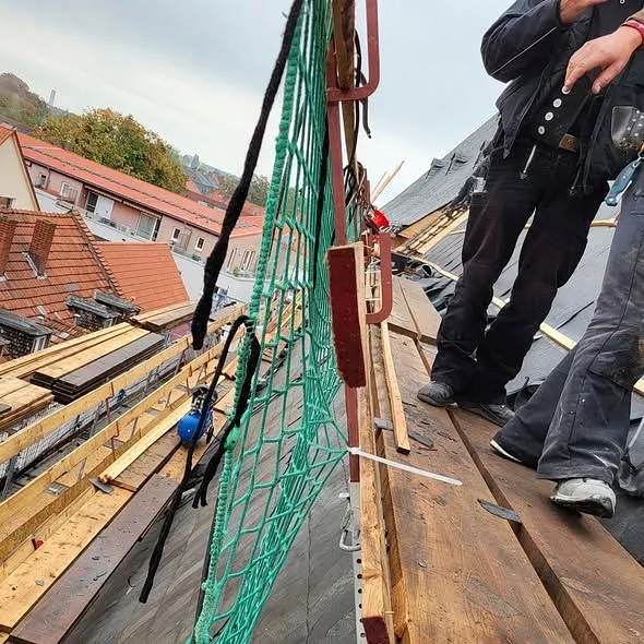 Bild vom Baugerüst auf dem Dach, es sind die Beine von Dachdeckern zu sehen, die über Holzbohlen laufen.
