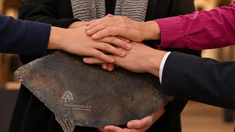 Verschiedene Hände gemeinsam auf einem symbolischen Dachschiefer der Marienkirche