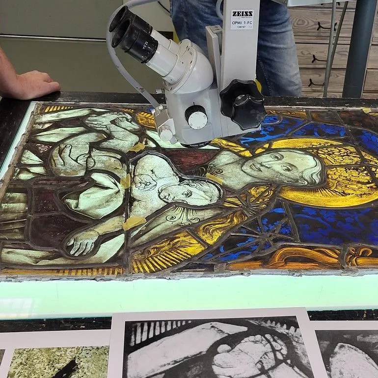 Ein Vergrößerungsglas hängt über dem Buntglasfeld von Johannes dem Täufer.